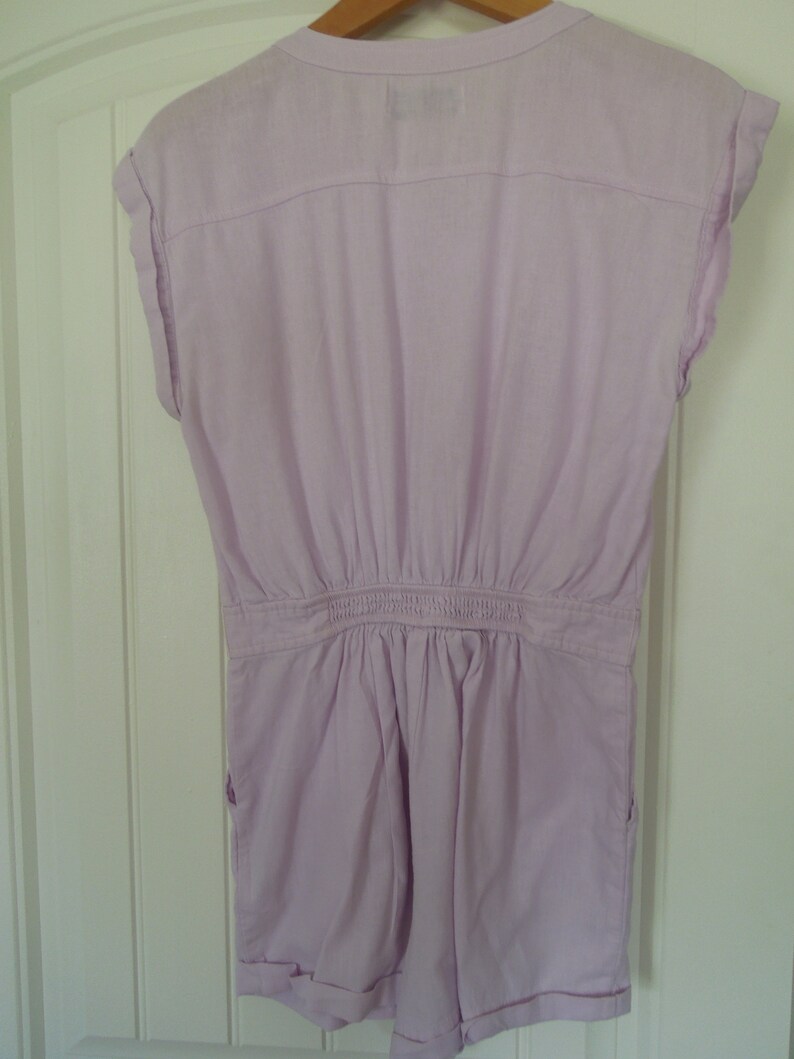 May include: A light purple short-sleeved jumpsuit with a button-up front and a gathered waist.