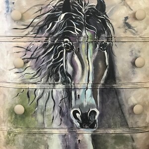 Puede incluir: Una c&oacute;moda blanca con cuatro cajones pintados con una cabeza de caballo en blanco y negro. Cada caj&oacute;n tiene un pomo redondo.