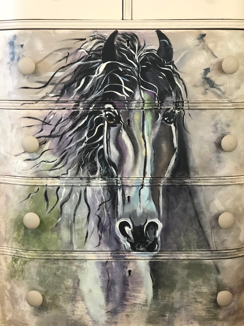 Puede incluir: Una c&oacute;moda blanca con cuatro cajones pintados con una cabeza de caballo en blanco y negro. Cada caj&oacute;n tiene un pomo redondo.