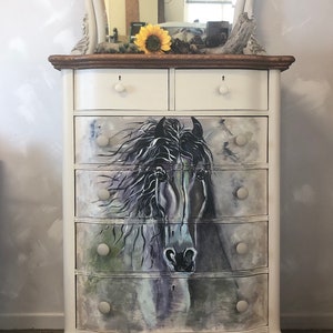 Puede incluir: C&oacute;moda blanca pintada con un espejo biselado en la parte superior. La c&oacute;moda tiene seis cajones con pomos blancos y una imagen pintada de una cabeza de caballo en la parte delantera.