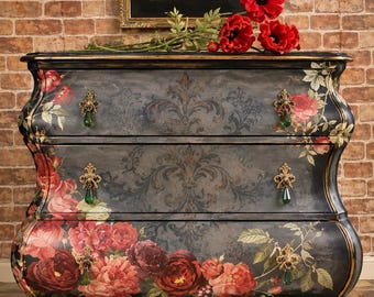 May include: A three-drawer chest featuring a dark gray finish with a black damask pattern and large red floral motifs. The piece includes ornate gold-toned metal hardware with dangling green teardrop accents and curved side profiles.