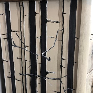 Puede incluir: Primer plano de la parte frontal de un caj&oacute;n de c&oacute;moda pintado con una escena de bosque en blanco y negro. El caj&oacute;n est&aacute; pintado con un fondo beige claro y presenta rayas negras verticales que representan &aacute;rboles. Los &aacute;rboles est&aacute;n acentuados con finas ramas blancas.