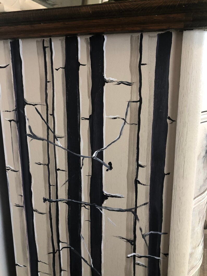 Puede incluir: Primer plano de la parte frontal de un caj&oacute;n de c&oacute;moda pintado con una escena de bosque en blanco y negro. El caj&oacute;n est&aacute; pintado con un fondo beige claro y presenta rayas negras verticales que representan &aacute;rboles. Los &aacute;rboles est&aacute;n acentuados con finas ramas blancas.