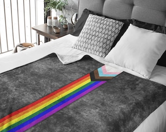 May include: A gray fleece throw blanket with a rainbow stripe and a black, brown, light blue, pink, and white chevron pattern. The blanket is on a bed with white and gray pillows.