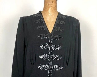 May include: A black dress with a V-neckline and long sleeves. The dress is decorated with a vertical design of black sequins.