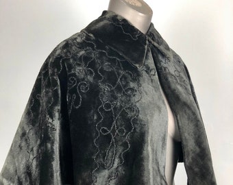 May include: A black velvet cape with a collar and beaded embroidery. The cape is short and has a flared shape.