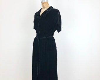 May include: A black velvet dress with a collared neckline and short sleeves. The dress has a fitted bodice and a flowing skirt.