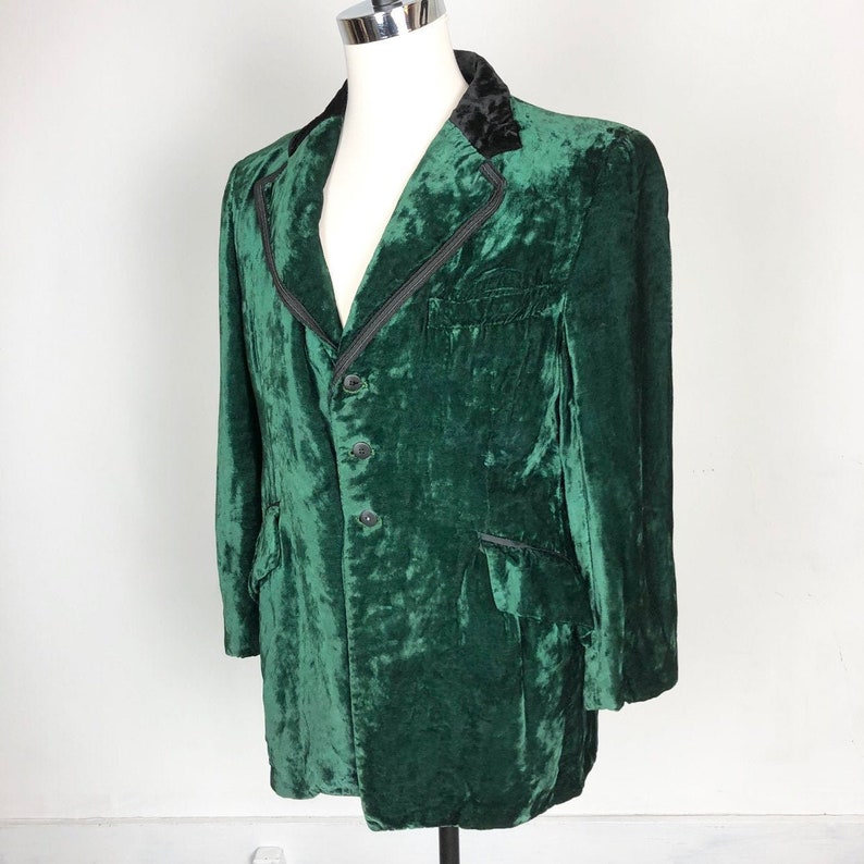 May include: A dark green velvet blazer with a black velvet collar and four black buttons. The blazer has a classic cut and a slightly longer length.