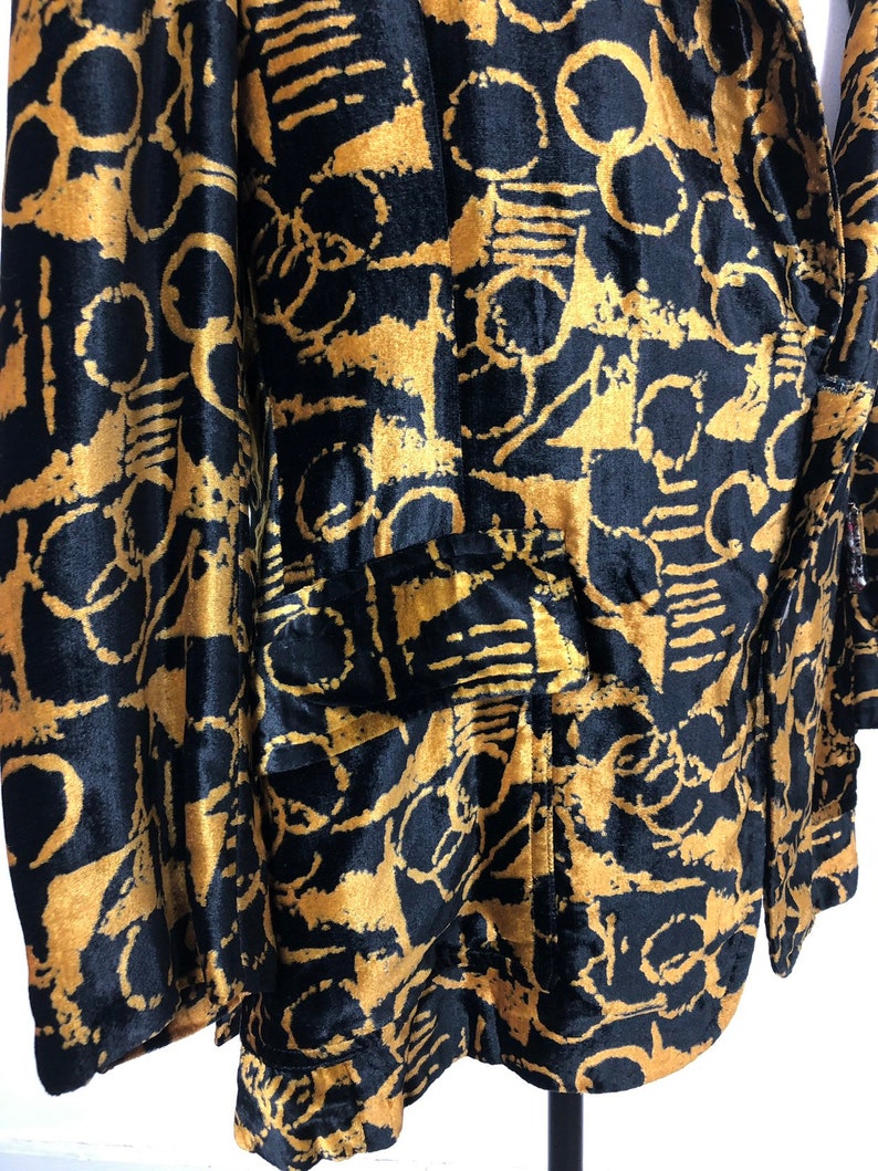 May include: A black velvet blazer with a gold abstract print. The blazer has a single button closure and two pockets.