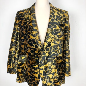 May include: A black and gold blazer with a geometric pattern. The blazer has a single button closure and two pockets.