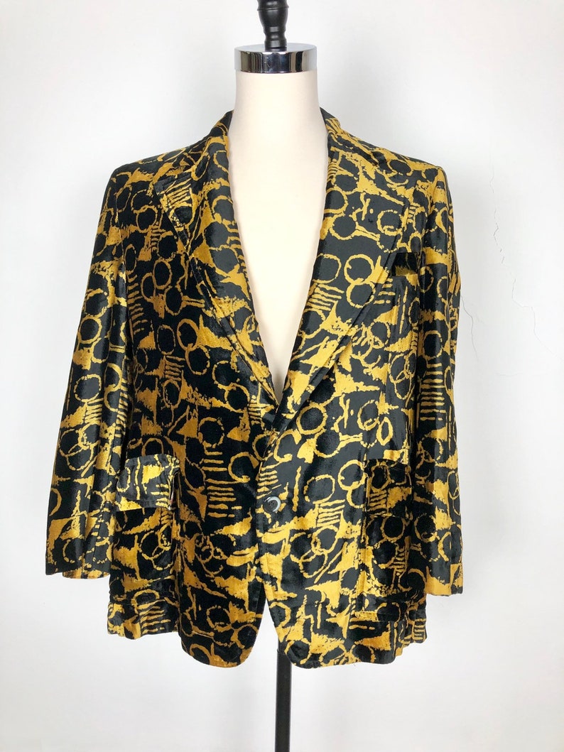 May include: A black and gold blazer with a geometric pattern. The blazer has a single button closure and two pockets.