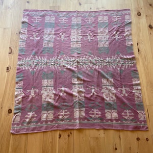 May include: A pink and white woven blanket with a geometric pattern featuring stylized figures. The blanket has a traditional Native American design.
