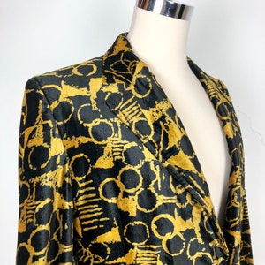 May include: A black velvet blazer with a gold abstract pattern. The blazer has a notched collar and a single button closure.