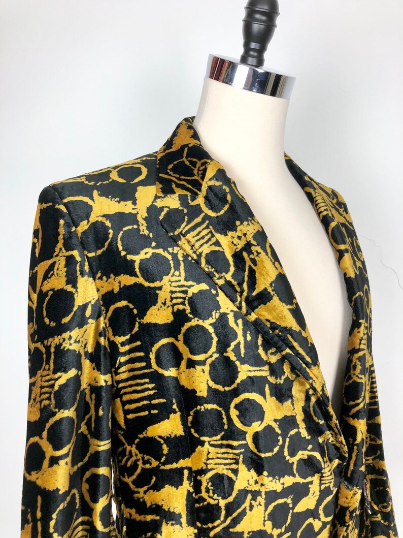 May include: A black velvet blazer with a gold abstract pattern. The blazer has a notched collar and a single button closure.