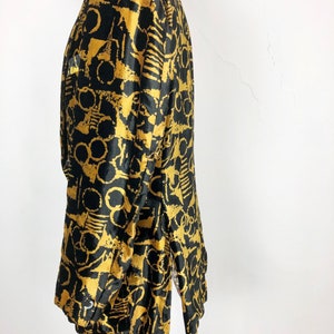 May include: A black and gold long-sleeved jacket with an abstract print. The jacket has a collar and a button closure.
