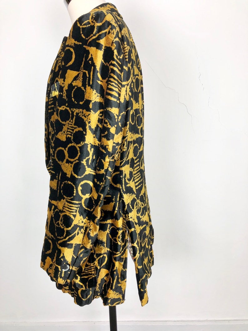 May include: A black and gold long-sleeved jacket with an abstract print. The jacket has a collar and a button closure.