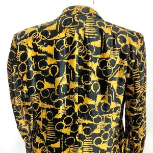 May include: A black velvet blazer with a gold abstract pattern. The pattern features circles, lines, and geometric shapes.