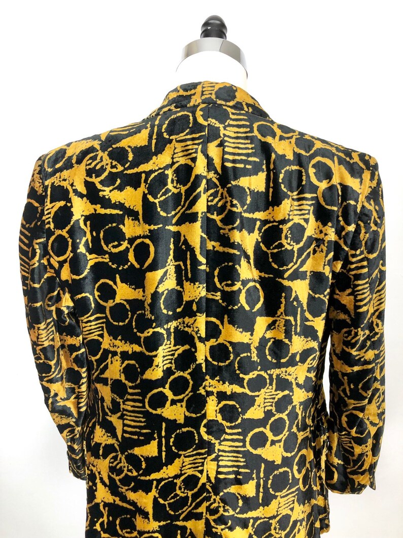May include: A black velvet blazer with a gold abstract pattern. The pattern features circles, lines, and geometric shapes.