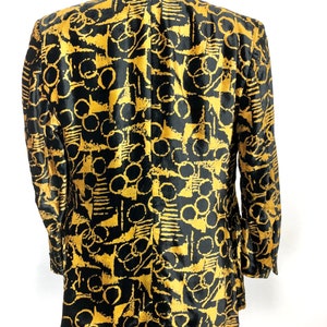 May include: A black blazer with a gold abstract pattern. The pattern features circles, lines, and geometric shapes.