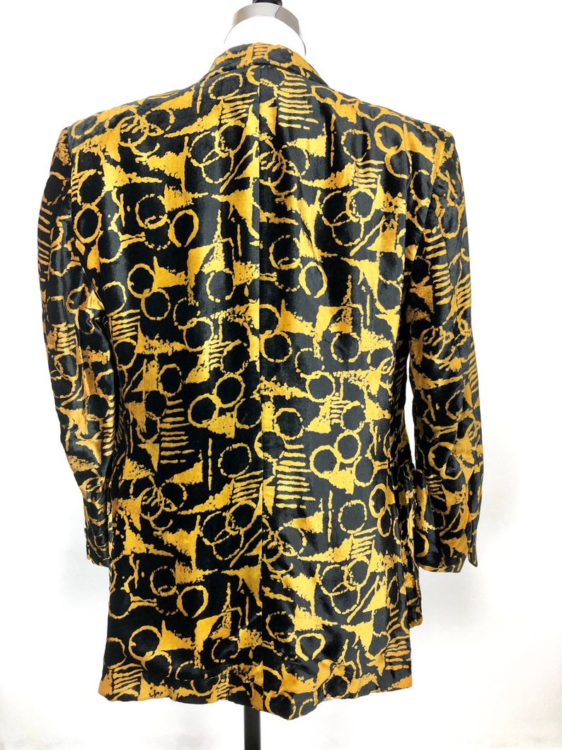 May include: A black blazer with a gold abstract pattern. The pattern features circles, lines, and geometric shapes.