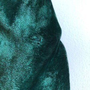 May include: Close-up of a dark green velvet fabric with a small hole in the center.