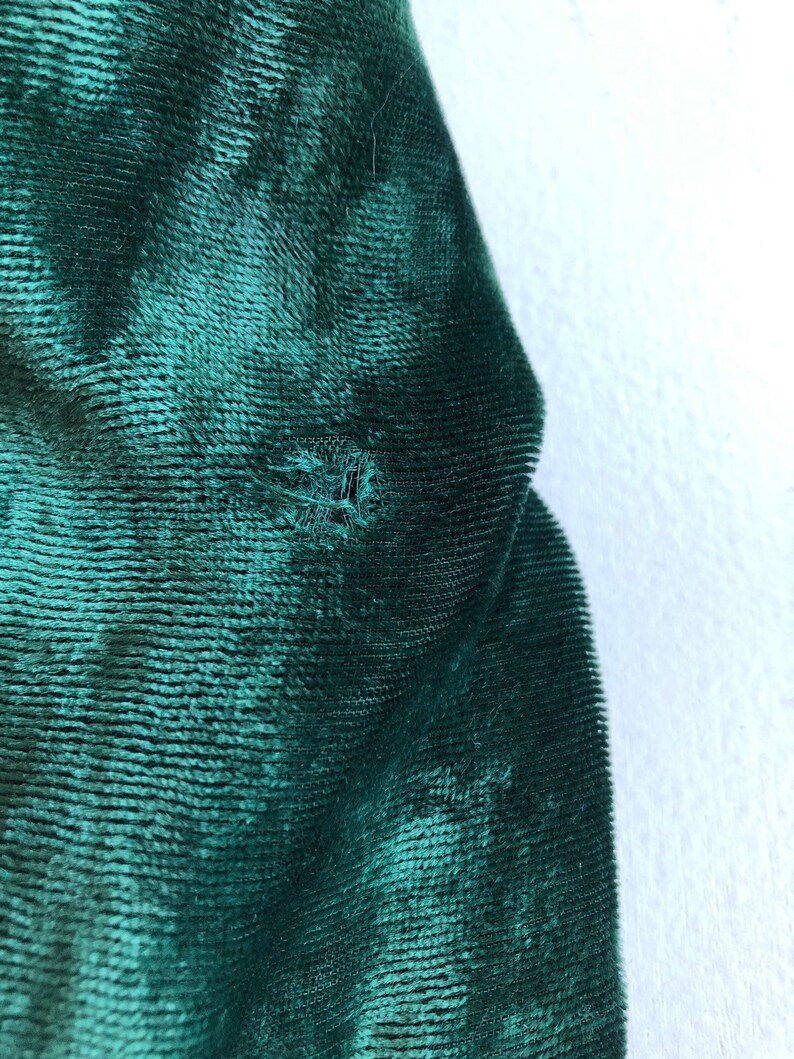 May include: Close-up of a dark green velvet fabric with a small hole in the center.