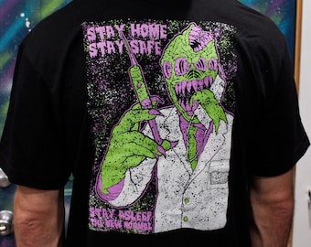 May include: Black t-shirt featuring a graphic print of a green monster wearing a white lab coat and holding a syringe. The text "Stay Home Stay Safe Stay Asleep The New Normal" is printed on the shirt.