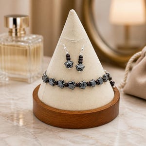 May include: A jewelry set consisting of a bracelet and a pair of drop earrings. Both pieces feature dark metallic star-shaped beads alternating with small dark brown spherical beads, finished with silver-toned metal hooks on the earrings.
