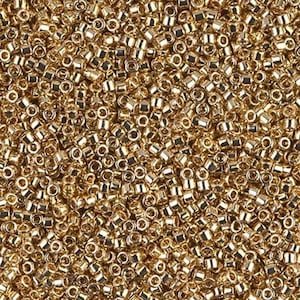 May include: Close-up of a pile of small, gold-colored seed beads. The beads are cylindrical with a hole running through the center, and they have a metallic sheen. The beads are densely packed together, creating a textured surface.