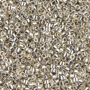 May include: A close-up view of a large quantity of silver-colored seed beads. The beads are small and round, with a hole in the center. They are arranged in a random pattern, creating a textured surface.