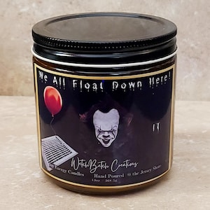 May include: A glass candle jar with a black lid features a horror-themed design. The label includes the text "We All Float Down Here!" with an image of a red balloon and a clown. The jar is 13oz.