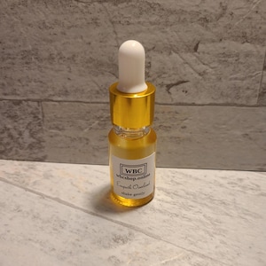 May include: A small, clear glass bottle with a gold cap and dropper. The bottle contains a yellow liquid and has a white label with the text "WBC wbcshop.online Empath Overload shake gently".