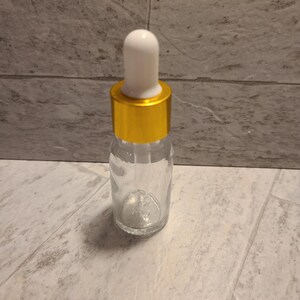 May include: A clear glass bottle with a gold lid and a white dropper. The bottle is empty.
