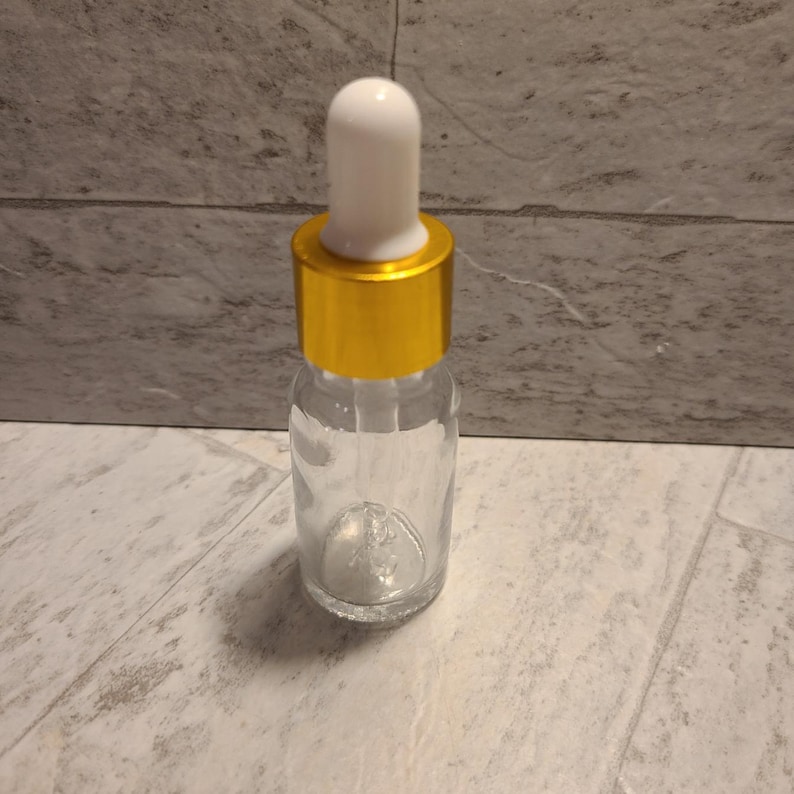 May include: A clear glass bottle with a gold lid and a white dropper. The bottle is empty.