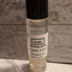 May include: A clear glass bottle with a black cap and a white label. The label reads "WBC wbcshop.online Candy Cane Kisses xx shake gently".