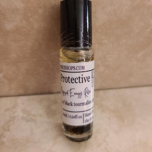 May include: A clear glass roller bottle with a black cap containing a light yellow liquid and dark particles. The white label reads WBCSHOPS.COM, Protective, Infused Energy Roller, w/ black tourmaline, 10ml / 0.34fl oz, Hand Crafted.