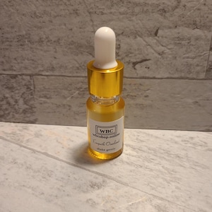 May include: A small, clear glass bottle with a gold cap and dropper. The bottle contains a yellow liquid and has a white label with the text "WBC wbcshop.online Empath Overload shake gently".