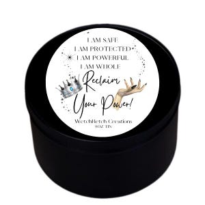 May include: A black 8 oz tin with a white label. The label features the text "I AM SAFE, I AM PROTECTED, I AM POWERFUL, I AM WHOLE" and "Reclaim Your Power!". A silver crown and a hand with a black nail are also on the label.