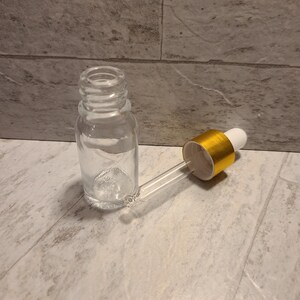 May include: A clear glass bottle with a gold-colored dropper cap. The bottle is empty and the dropper is detached.