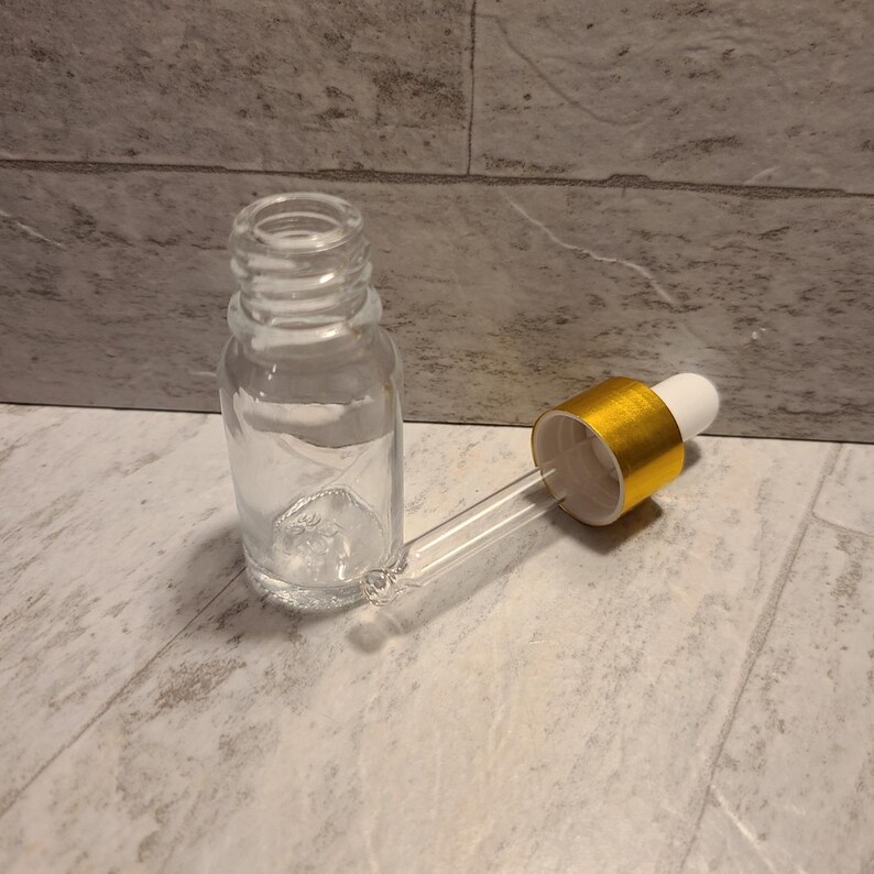 May include: A clear glass bottle with a gold-colored dropper cap. The bottle is empty and the dropper is detached.
