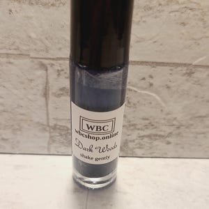 May include: A small, clear glass bottle with a black cap and a white label. The label says "WBC wbcshop.online Dark Woods shake gently".