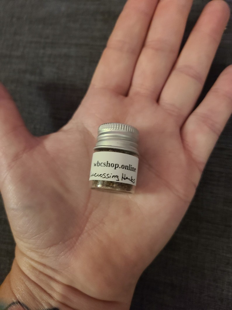 Puede incluir: Una peque&ntilde;a botella plateada con una etiqueta blanca que dice "wbshop.online" y "crossing herbs". La botella est&aacute; llena de hierbas marrones.