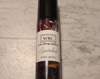 Puede incluir: Un frasco de vidrio transparente con aplicador de rodillo y tapa negra, lleno de un líquido rojo y pequeños trozos de flores secas. La etiqueta dice "WBC wbcshop.online Bewitched shake gently".