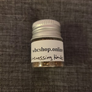 Puede incluir: Un peque&ntilde;o frasco plateado con una etiqueta blanca que dice "wbc shop.online" y "crossing herbs".