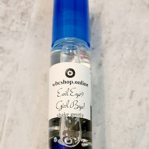 May include: A blue roller bottle with a white label that reads "wbcshop.online Evil Eye? Girl Bye! shake gently". The label also features a blue and white evil eye symbol.