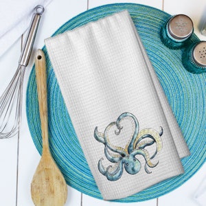 May include: White kitchen towel with a blue and yellow octopus illustration. The octopus has its tentacles curled into a heart shape.