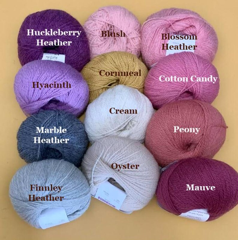 Puede incluir: Una colecci&oacute;n de ovillos de lana en varios colores, incluyendo morado, rosa, amarillo y gris. Cada ovillo est&aacute; etiquetado con su nombre de color, como "Huckleberry Heather", "Blush" y "Finnley Heather". La lana est&aacute; dispuesta sobre un fondo amarillo.