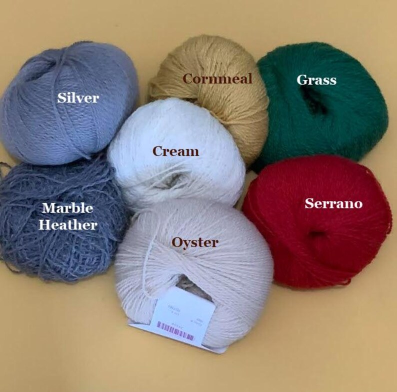 Puede incluir: Una colecci&oacute;n de ovillos de lana en varios colores, incluyendo plata, ma&iacute;z, hierba, crema, m&aacute;rmol brezo, ostra y serrano. Cada ovillo est&aacute; etiquetado con su nombre de color, ofreciendo una gu&iacute;a visual para proyectos de manualidades. La lana est&aacute; dispuesta sobre una superficie amarillo claro.