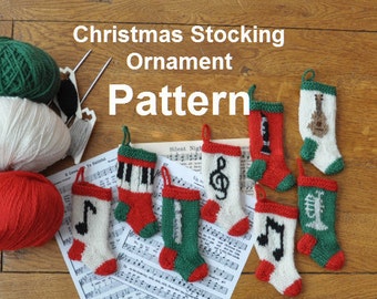 Könnte beinhalten: Eine Sammlung von acht gestrickten Weihnachtsstrumpf-Ornamenten mit verschiedenen musikalischen Themen. Die Ornamente sind weiß mit roten und grünen Akzenten und zeigen Designs wie ein Klavier, einen Violinschlüssel, einen Bassschlüssel, Noten, eine Klarinette, eine Gitarre und eine Glocke. Die Ornamente werden auf einem Notenblatt mit dem Titel "Stille Nacht" gezeigt.