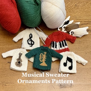 May include: Five miniature knitted sweaters with musical notes and instruments, including a treble clef, piano keys, guitar, trumpet, and a music note. The sweaters are laid out on a wooden surface with balls of yarn in red, green, and white.